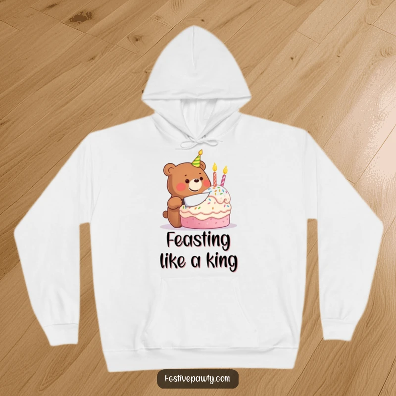 Funny hoodie depicting a beaming bear joyfully slicing into a large, festive birthday cake, combining comfort with celebration.